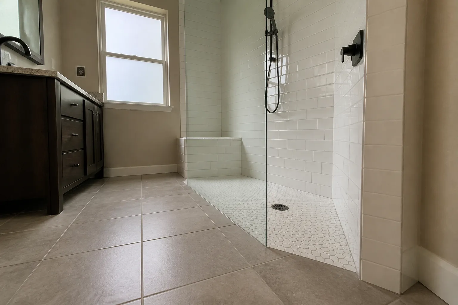 Curbless shower entry Low-angle view of a curbless walk-in shower entry, mosaic pan, tiled bench, and handheld shower on a slide bar